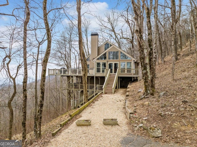 rear view of property featuring a deck, driveway, a chimney, and stairs