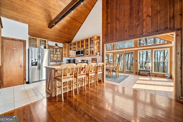 kitchen featuring high vaulted ceiling, wooden ceiling, light wood-style floors, appliances with stainless steel finishes, and glass insert cabinets