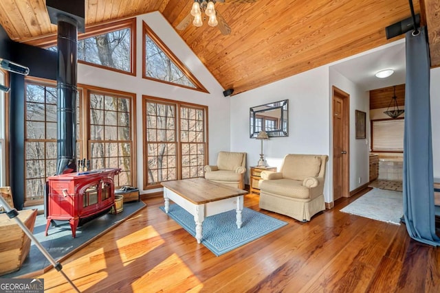 living area featuring high vaulted ceiling, a wood stove, wooden ceiling, and wood finished floors