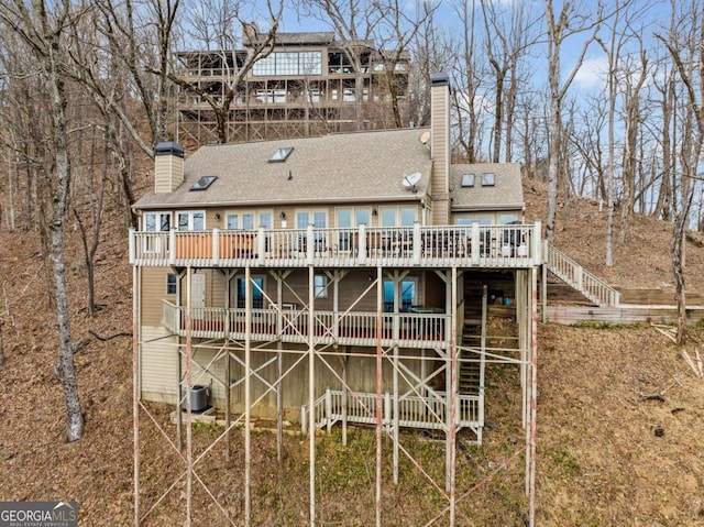 rear view of property featuring a deck, central air condition unit, a shingled roof, stairs, and a chimney