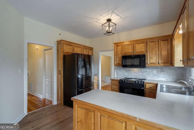 kitchen with a peninsula, a sink, light countertops, backsplash, and black appliances