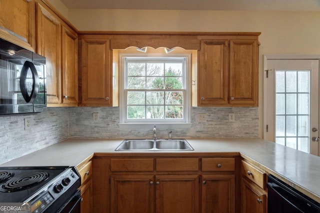 kitchen with brown cabinets, a sink, light countertops, black appliances, and backsplash