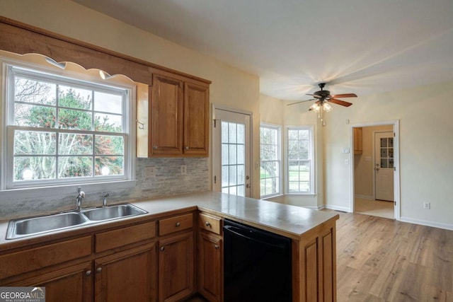 kitchen with black dishwasher, brown cabinets, a peninsula, a healthy amount of sunlight, and a sink