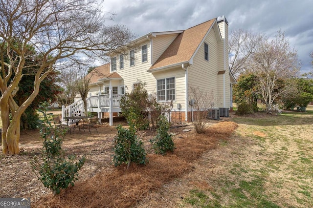 view of side of home with roof with shingles, central AC unit, a chimney, and a wooden deck