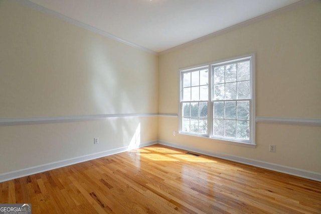 unfurnished room featuring ornamental molding, wood finished floors, visible vents, and baseboards