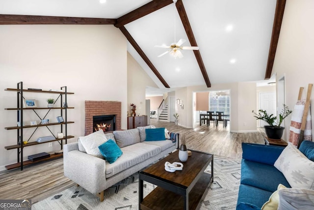 living room with wood finished floors, beamed ceiling, high vaulted ceiling, stairs, and a brick fireplace