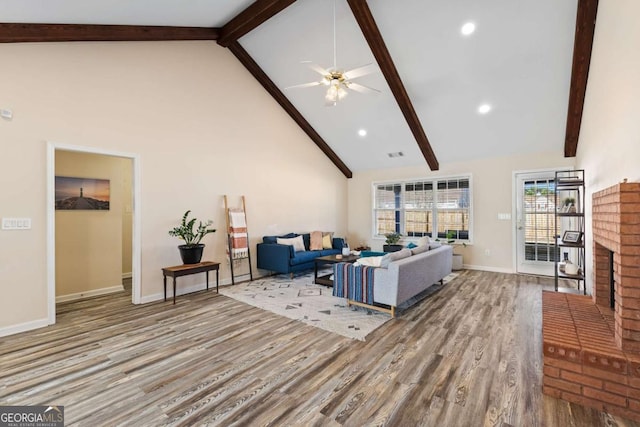 living room with beamed ceiling, a brick fireplace, high vaulted ceiling, and wood finished floors