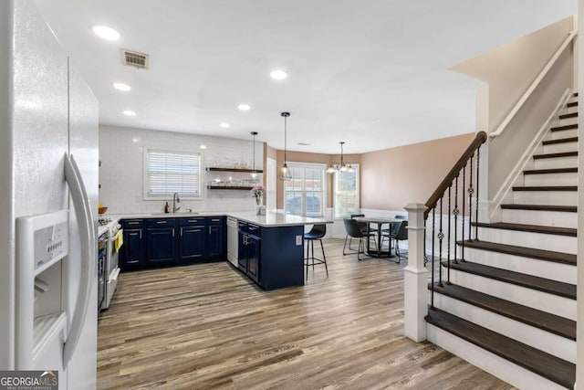 kitchen featuring visible vents, blue cabinetry, a peninsula, white fridge with ice dispenser, and a sink