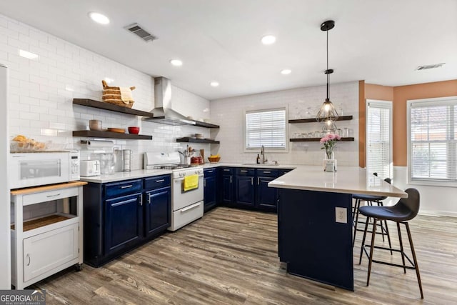 kitchen featuring blue cabinets, a peninsula, white appliances, wall chimney exhaust hood, and open shelves