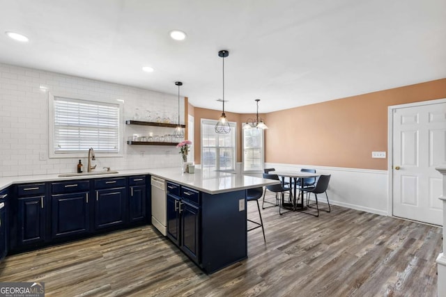 kitchen with blue cabinets, a breakfast bar, a sink, a peninsula, and white dishwasher