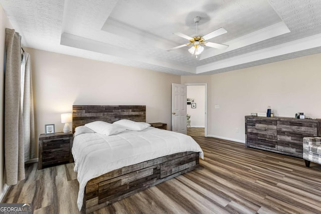 bedroom with a textured ceiling, a raised ceiling, and wood finished floors