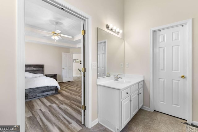 bathroom with baseboards, wood finished floors, vanity, a raised ceiling, and a ceiling fan