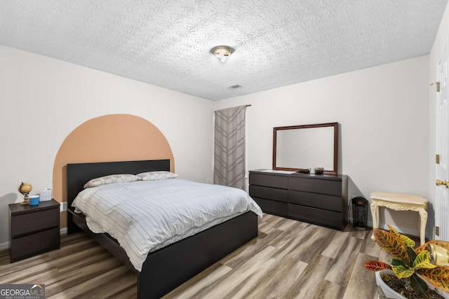 bedroom featuring a textured ceiling, baseboards, and wood finished floors