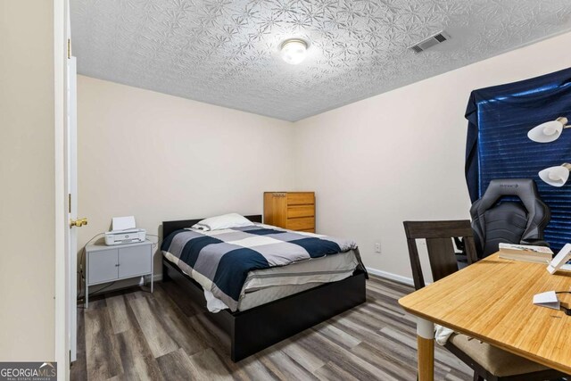 bedroom featuring visible vents, a textured ceiling, baseboards, and wood finished floors