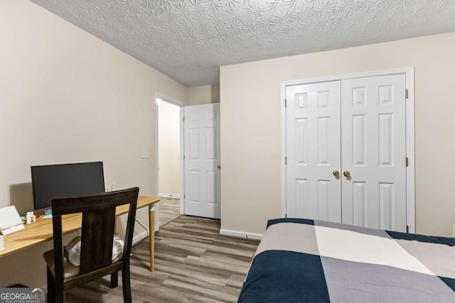 bedroom featuring a closet, a textured ceiling, baseboards, and wood finished floors