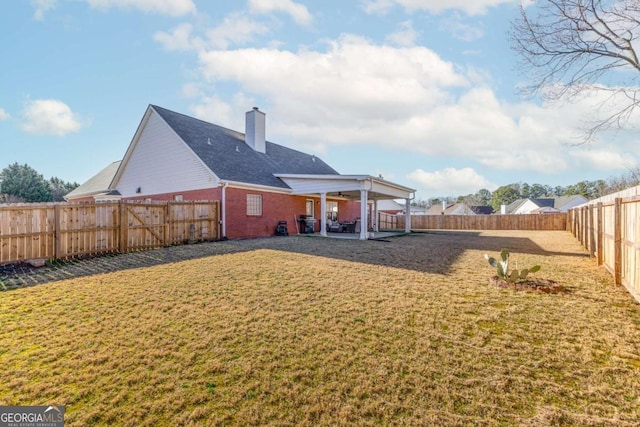 back of house featuring a lawn, a chimney, a fenced backyard, and brick siding