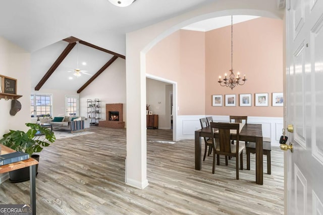 dining space featuring a decorative wall, ceiling fan with notable chandelier, a brick fireplace, and light wood-style floors