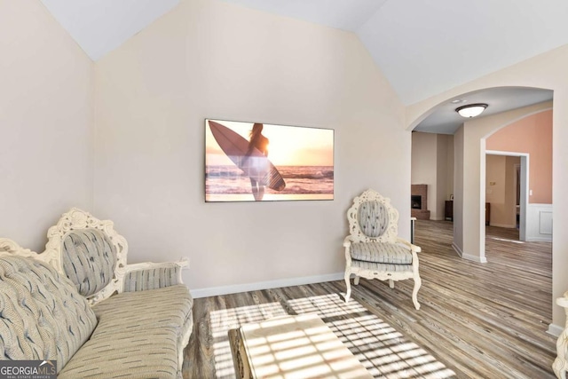 living area with wood finished floors, baseboards, lofted ceiling, a fireplace, and arched walkways