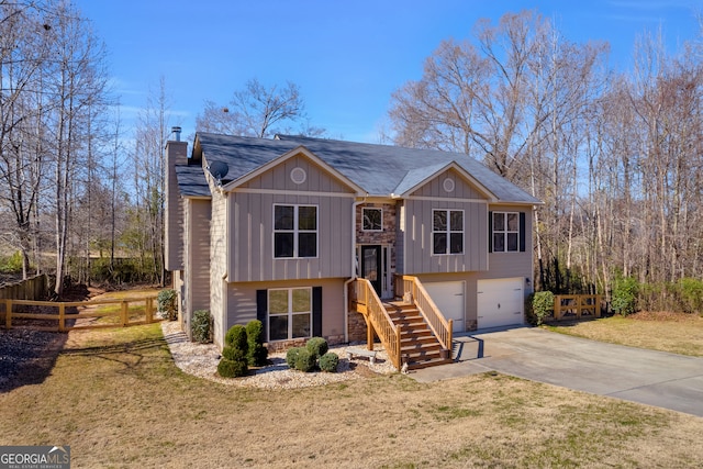 bi-level home with a chimney, a front yard, fence, a garage, and driveway