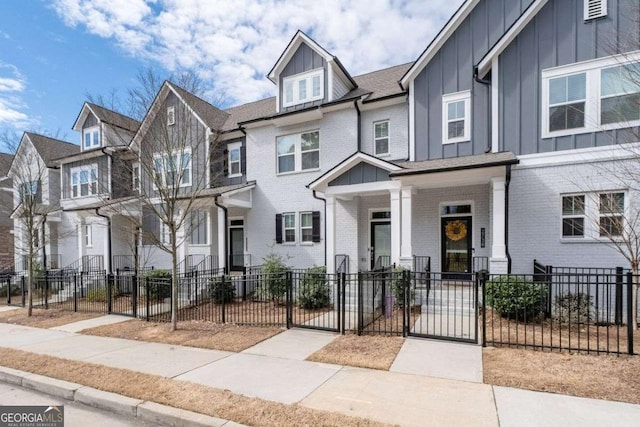 townhome / multi-family property featuring a fenced front yard, brick siding, covered porch, board and batten siding, and a gate