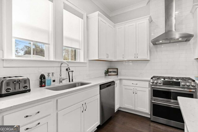 kitchen featuring stainless steel appliances, ornamental molding, white cabinetry, a sink, and wall chimney exhaust hood