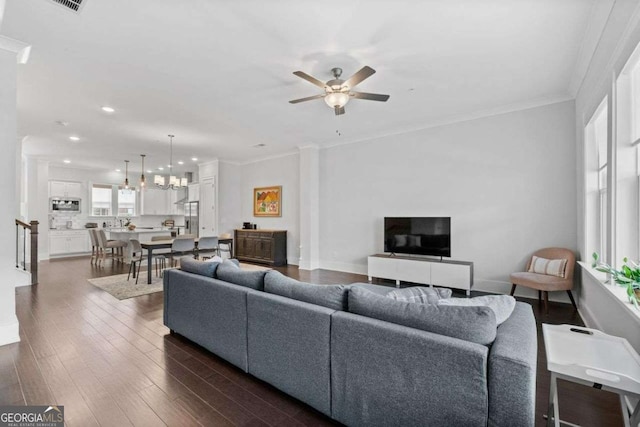 living area featuring dark wood-style floors, baseboards, ornamental molding, and ceiling fan with notable chandelier