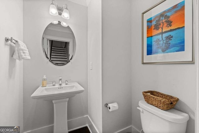 half bath with toilet, baseboards, and a sink