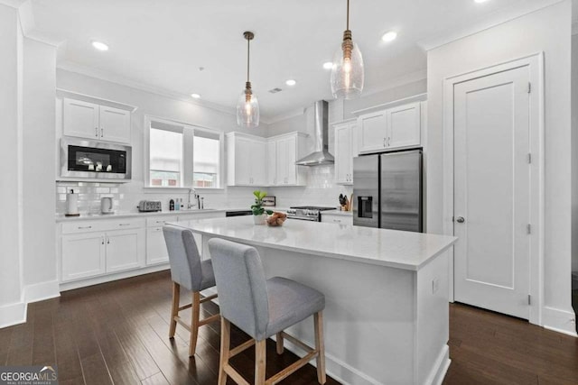 kitchen with stainless steel appliances, wall chimney range hood, a sink, and white cabinetry