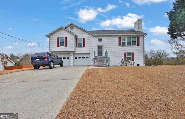 raised ranch featuring concrete driveway, a front lawn, a chimney, and an attached garage