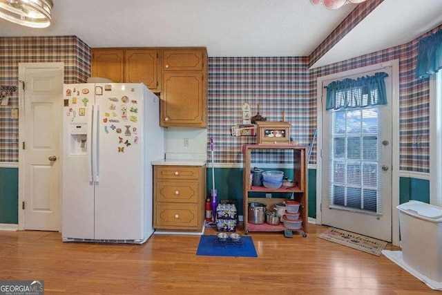 kitchen featuring light countertops, white refrigerator with ice dispenser, light wood-style flooring, and wallpapered walls