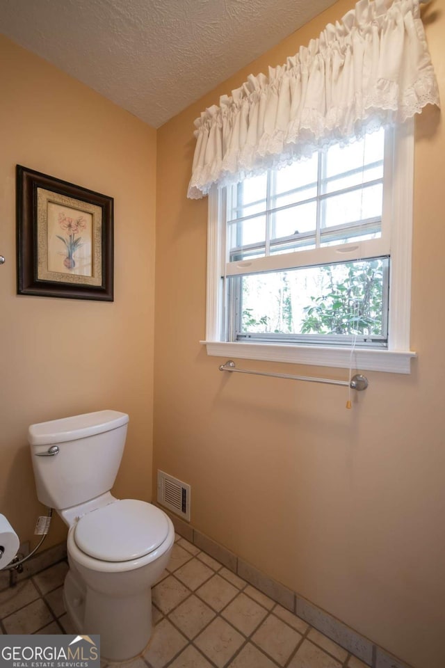 bathroom featuring baseboards, visible vents, toilet, tile patterned flooring, and a textured ceiling