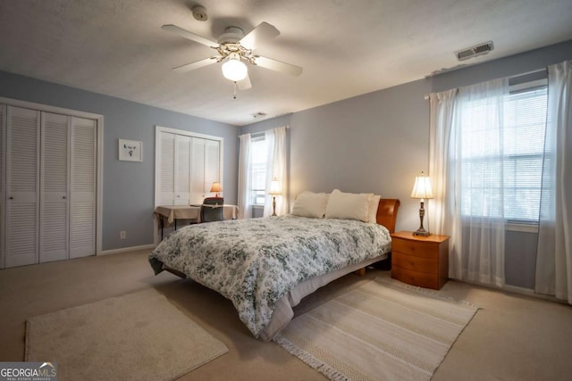 bedroom with light carpet, a ceiling fan, visible vents, baseboards, and two closets