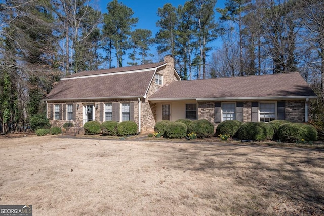 dutch colonial with brick siding, roof with shingles, a chimney, a gambrel roof, and a front yard