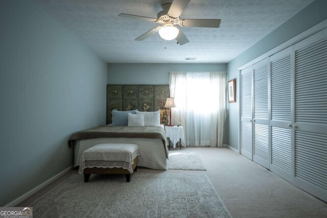 carpeted bedroom with a closet, visible vents, a ceiling fan, a textured ceiling, and baseboards