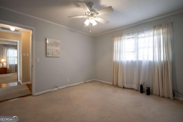 empty room featuring light carpet, baseboards, a ceiling fan, and crown molding