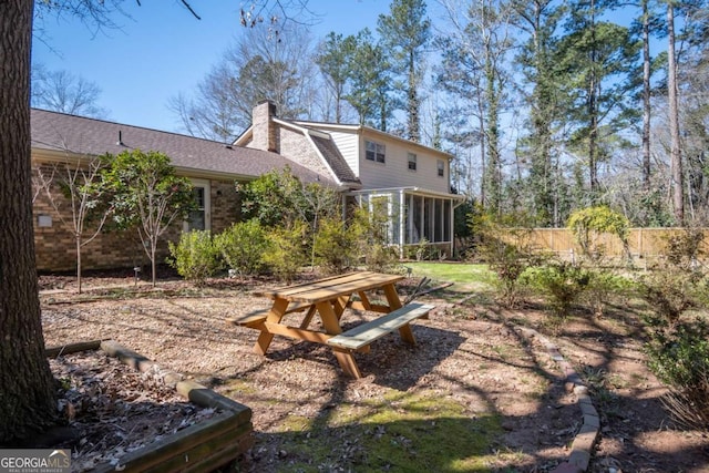 rear view of property featuring brick siding, roof with shingles, a chimney, a sunroom, and fence