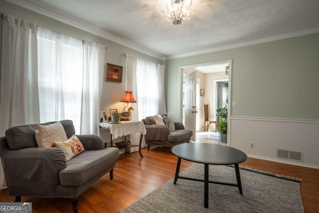 living area with a wainscoted wall, visible vents, crown molding, and wood finished floors