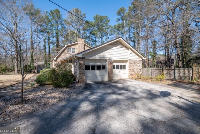 view of home's exterior featuring brick siding, a chimney, an attached garage, fence, and driveway