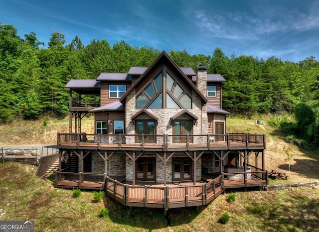 back of house featuring stone siding, a wooden deck, a chimney, and french doors