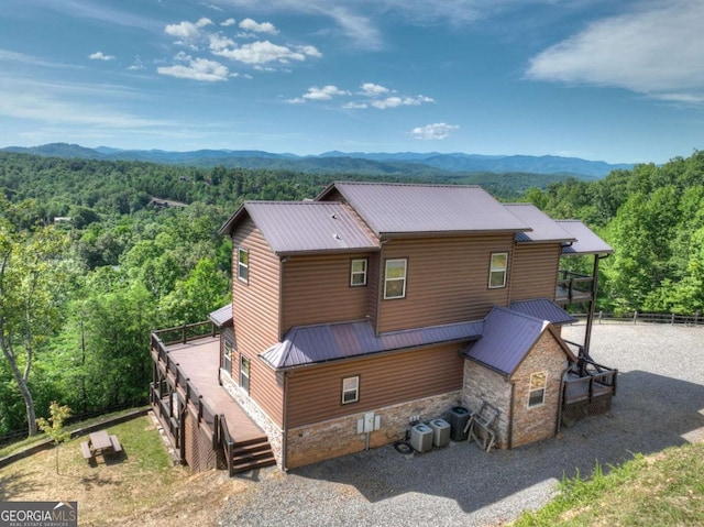 rear view of property with stone siding, central AC, metal roof, and a forest view