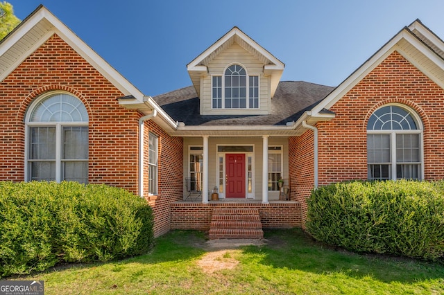 view of front of house featuring brick siding, a porch, a shingled roof, and a front yard