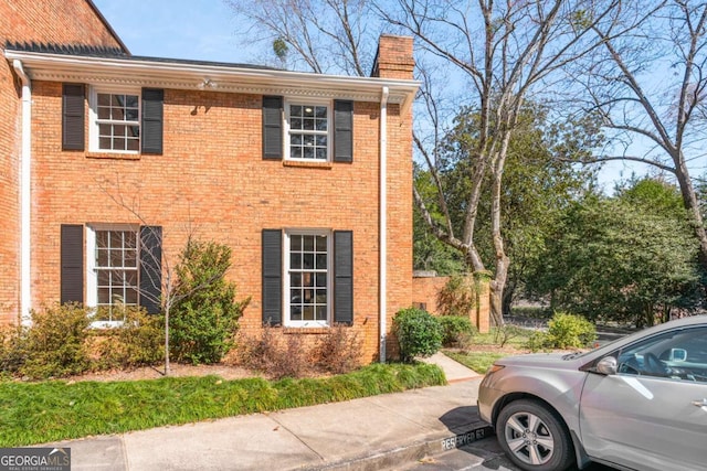 view of home's exterior with uncovered parking, brick siding, and a chimney