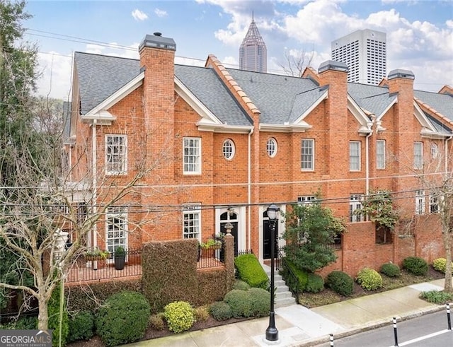 view of front of property featuring brick siding, a chimney, and a shingled roof