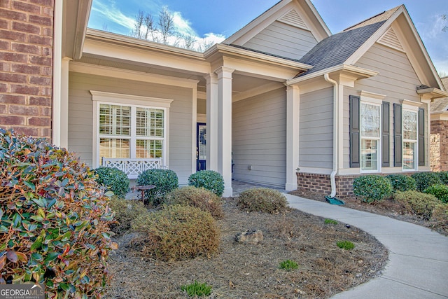 entrance to property with covered porch, brick siding, and roof with shingles