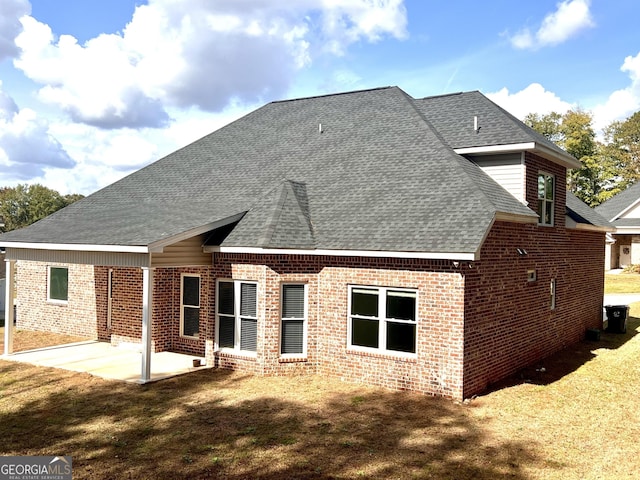 back of house with a patio, brick siding, a lawn, and a shingled roof