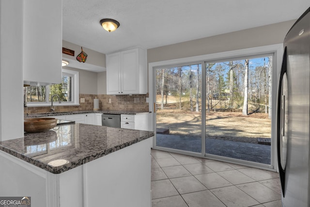 kitchen featuring dark stone countertops, a sink, appliances with stainless steel finishes, white cabinetry, and tasteful backsplash