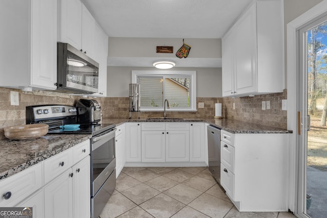 kitchen with backsplash, dark stone countertops, appliances with stainless steel finishes, white cabinets, and a sink