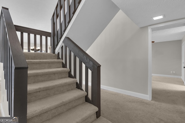 stairway featuring carpet, baseboards, and a textured ceiling