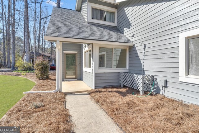 view of exterior entry with a yard and roof with shingles