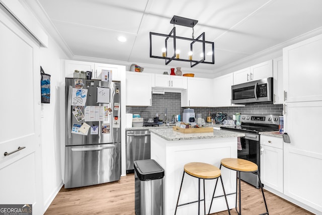 kitchen with appliances with stainless steel finishes, light wood-type flooring, a kitchen island, and crown molding